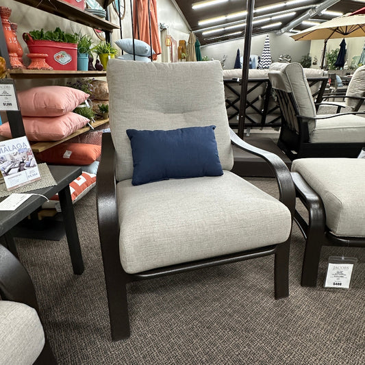 Gray chair with a blue pillow in a store setting with other furniture and decor items.