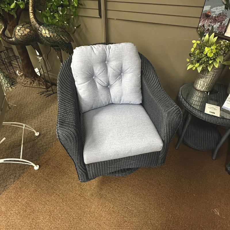 Wicker chair with gray cushions on a brown carpeted floor.