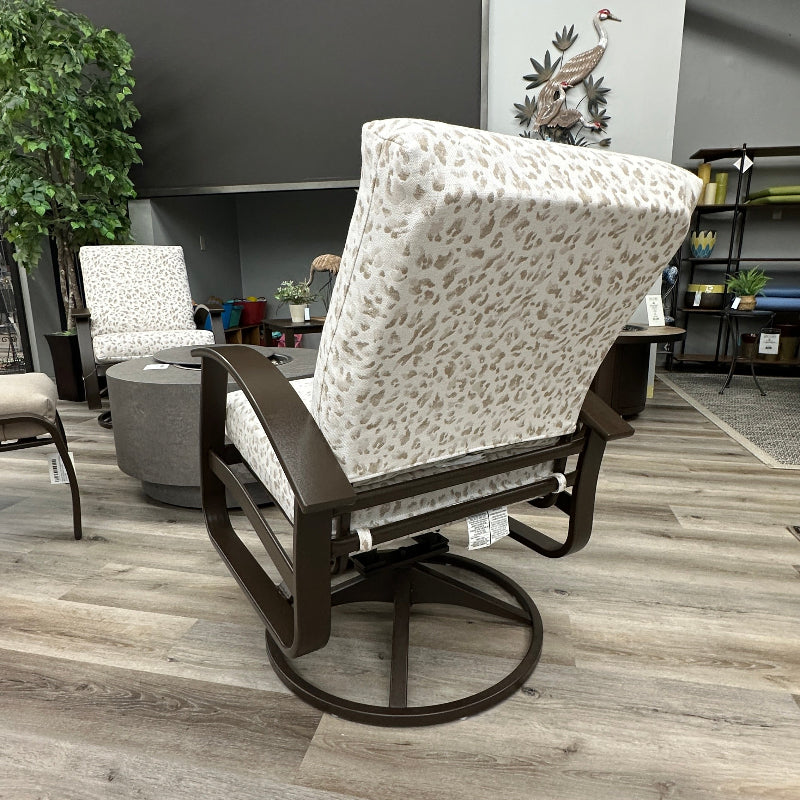 A modern rocking chair with a dark brown wooden frame and cream fabric upholstery featuring a small brown animal print, shown in a furniture showroom on a wood-look floor.
