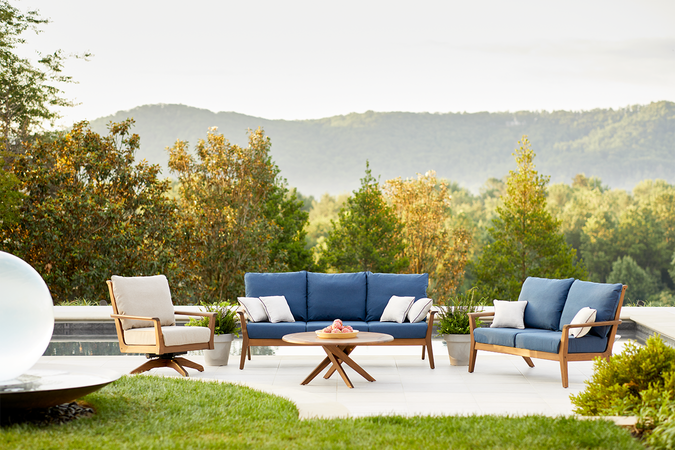 Outdoor furniture set with blue cushions and wooden frames in a scenic setting with trees and mountains.