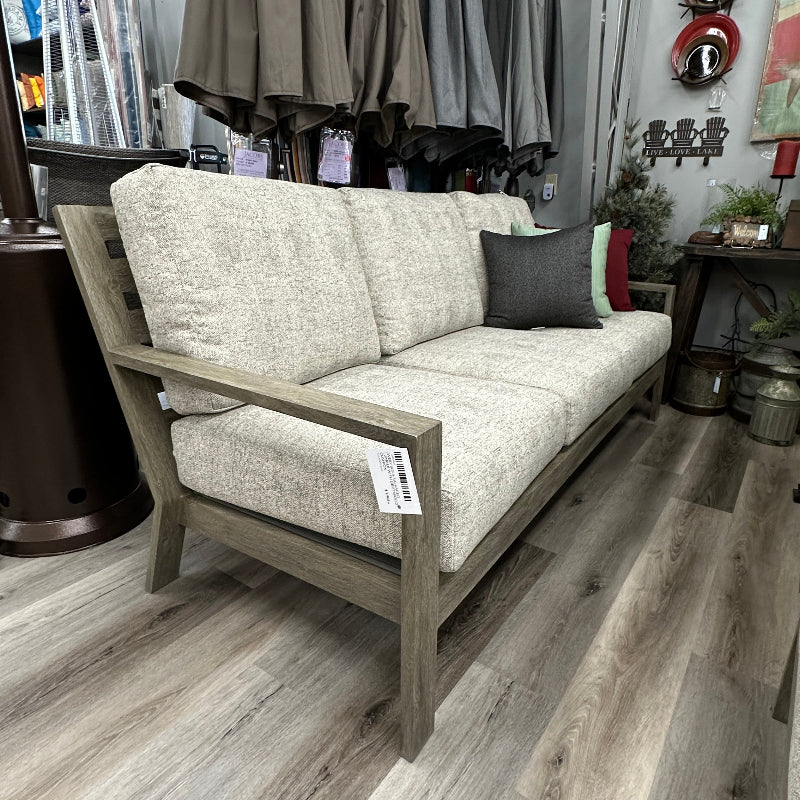 Gray sofa with cushions in a store setting with clothing racks in the background.