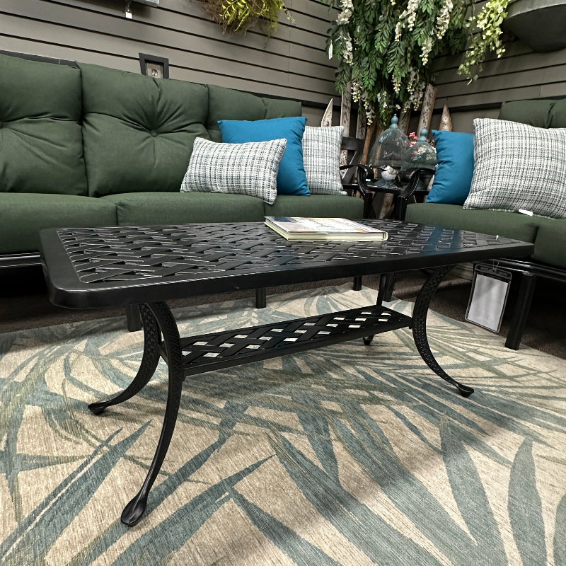 Outdoor patio with green cushioned sofa, black metal table, and decorative elements on a wooden deck.