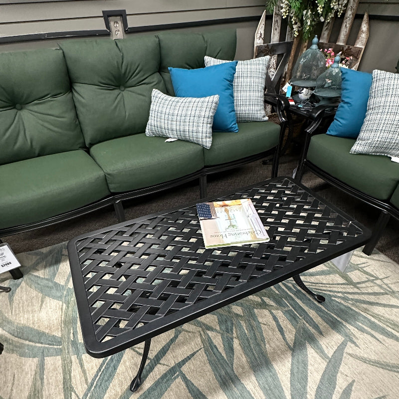 Outdoor patio setting with green sofa, black coffee table, and patterned rug.