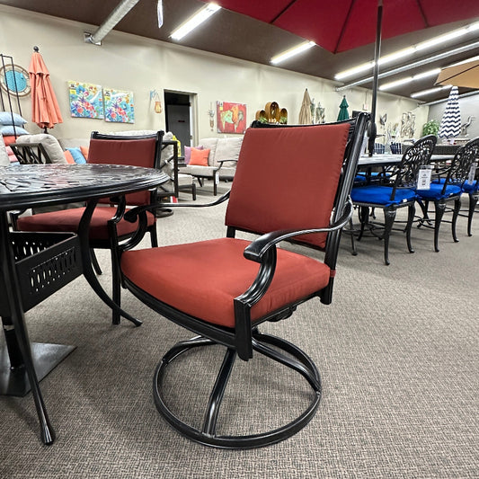 Red patio chair with black metal frame in a showroom setting with various furniture and decor items.