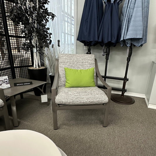 Chair with a green pillow in a room with umbrellas and a plant.