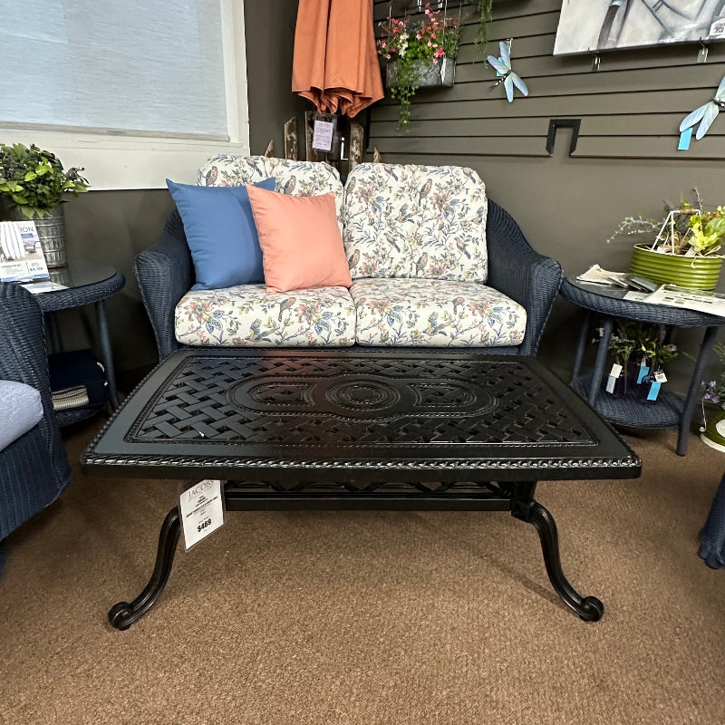 Outdoor furniture set with a black metal table and floral-patterned sofa against a wall.