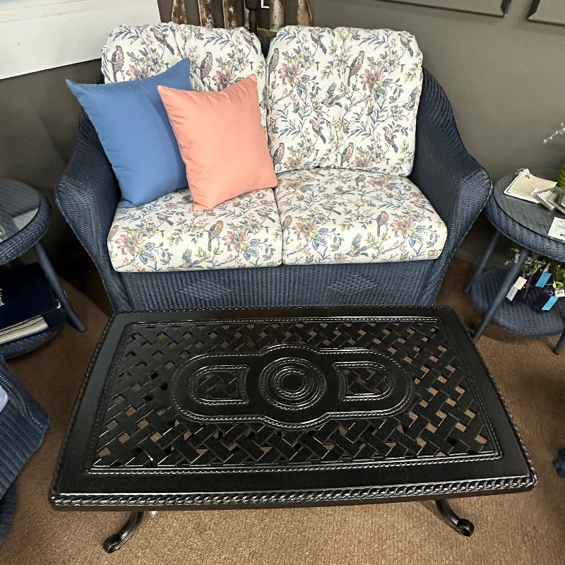 Wicker loveseat with floral cushions and decorative pillows in a room setting.