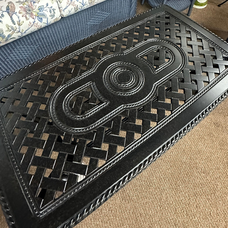 Black woven mat on a carpeted floor with a patterned sofa and side table in the background.