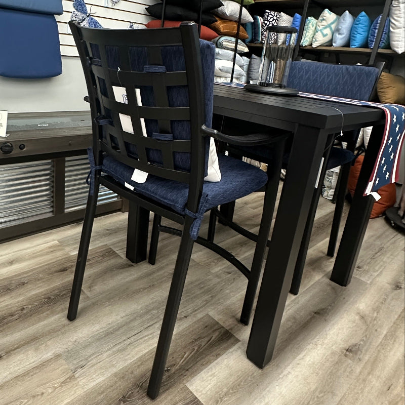 A dining table and matching chairs in a furniture showroom, with shelves of pillows and upholstery samples visible in the background.