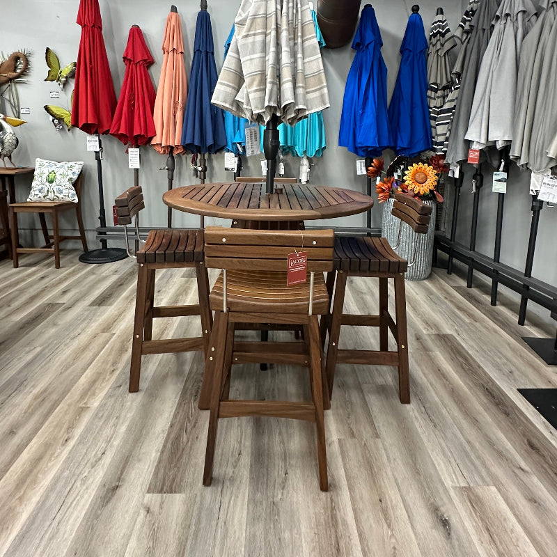 A wooden outdoor dining set consisting of a round slatted table and four matching bar stools, displayed in a furniture showroom with other patio umbrellas and decor in the background.