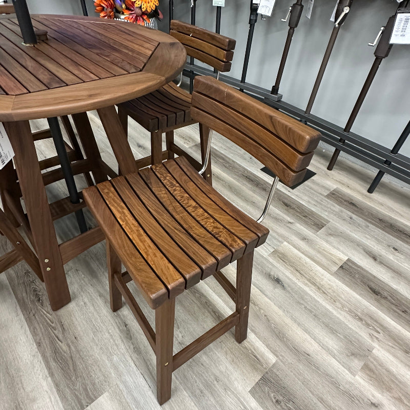 A 5-piece outdoor patio dining set featuring a round wooden table and four matching bar-height chairs with slatted backs and seats, shown on a gray wood-look floor in a retail store.