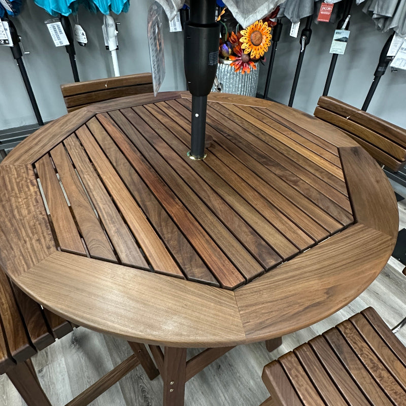 A round outdoor patio dining set with a brown wooden slatted table, matching chairs, and a gray striped umbrella in a store display.