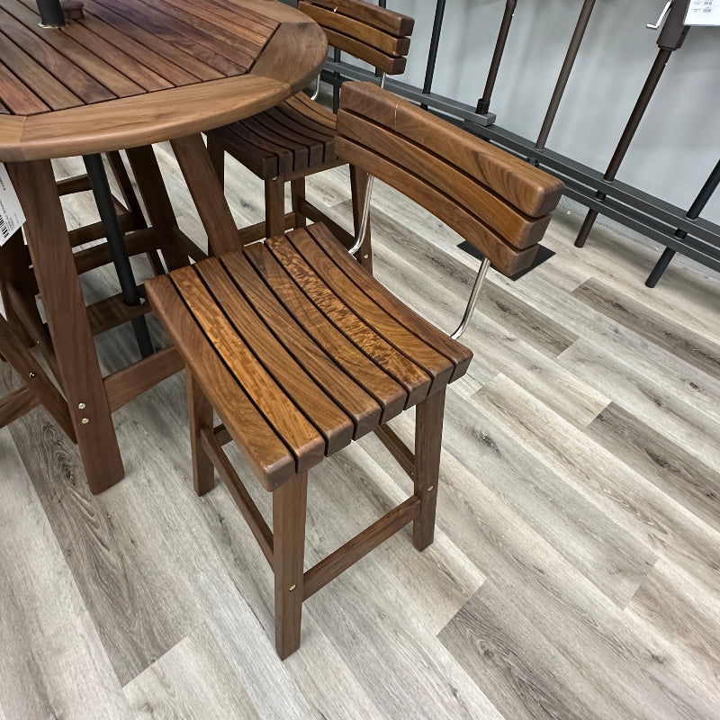 A 5-piece outdoor patio dining set featuring a round wooden table and four matching bar-height chairs with slatted backs and seats, shown on a gray wood-look floor in a retail store.