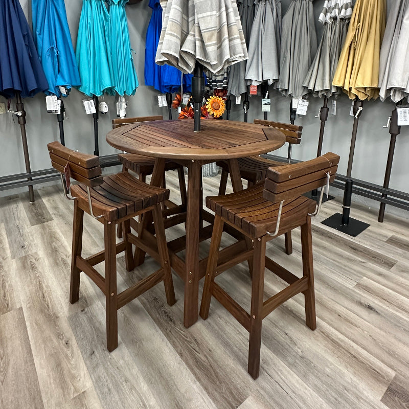 A 5-piece outdoor bar set consisting of a round wooden table and four matching wooden stools, displayed in a showroom with other patio umbrellas in the background.