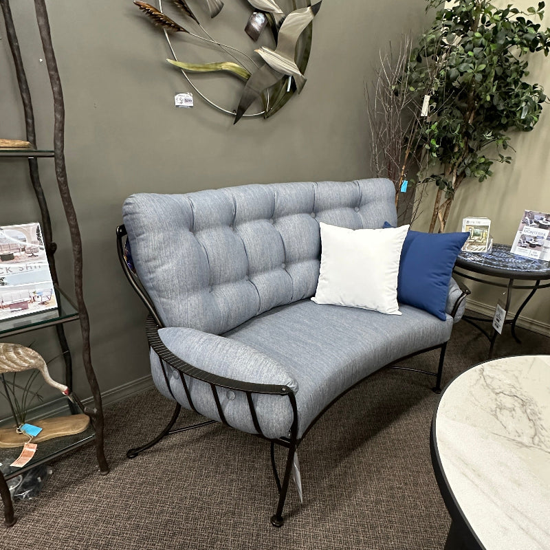 Gray cushioned bench with decorative pillows in a room setting with a wall art piece and plant.