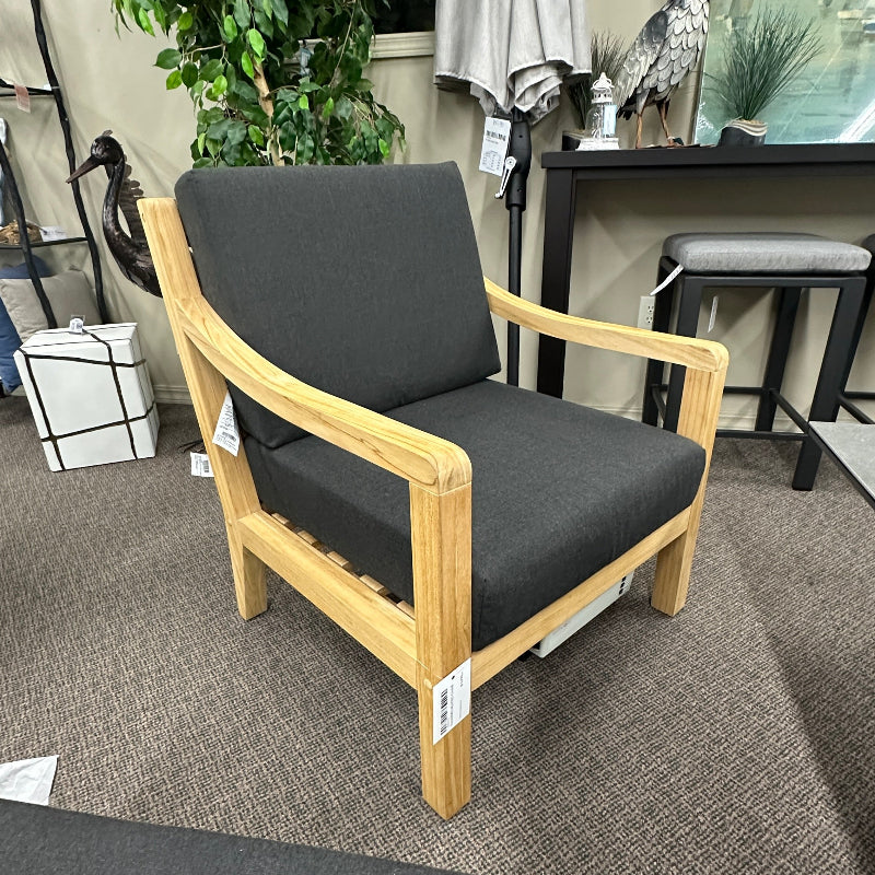 A modern lounge chair with a light natural wood frame and dark gray fabric cushions, shown in a furniture store setting.