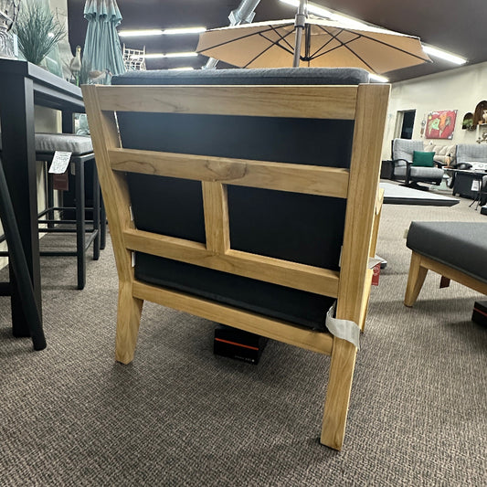 A wooden outdoor lounge chair with a black cushioned seat and backrest, shown from the rear in a furniture showroom.
