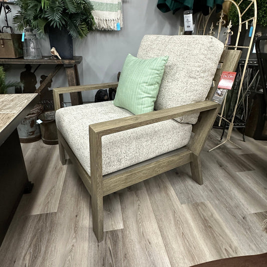 Chair with a light gray cushion and green pillow in a store setting with plants and furniture.