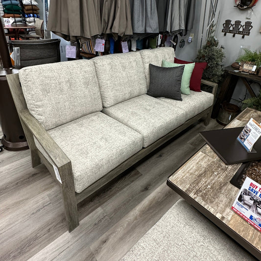 Outdoor furniture set with a sofa and table in a store setting, featuring hanging umbrellas in the background.