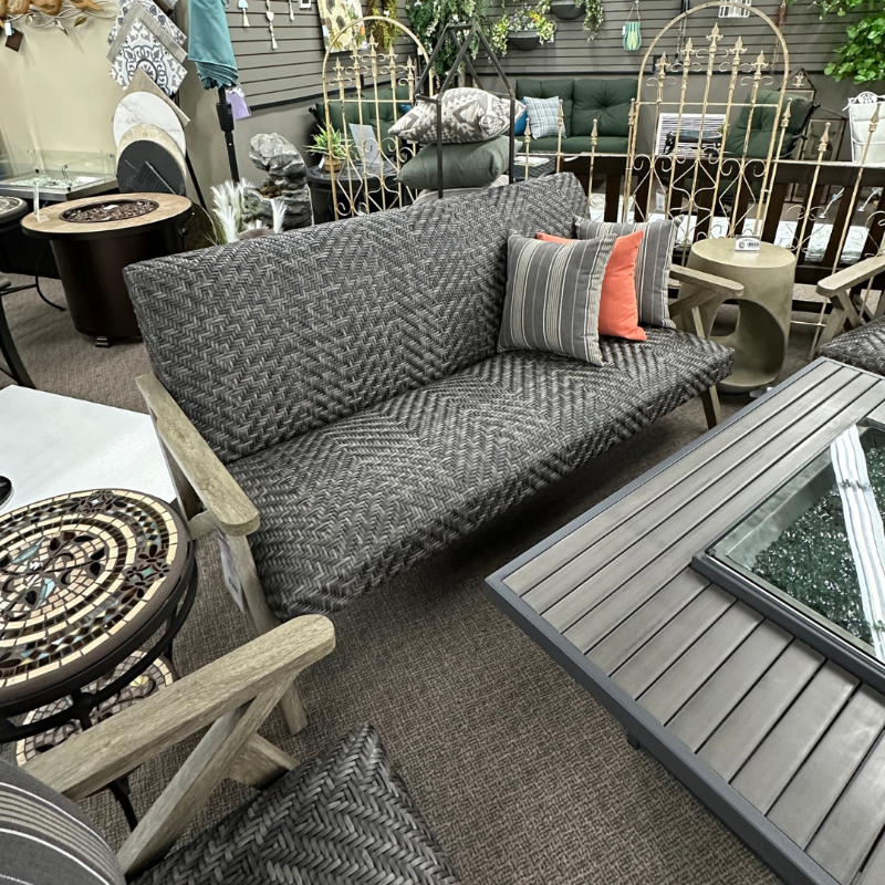 Gray sofa with patterned cushions in a showroom setting with various furniture pieces.