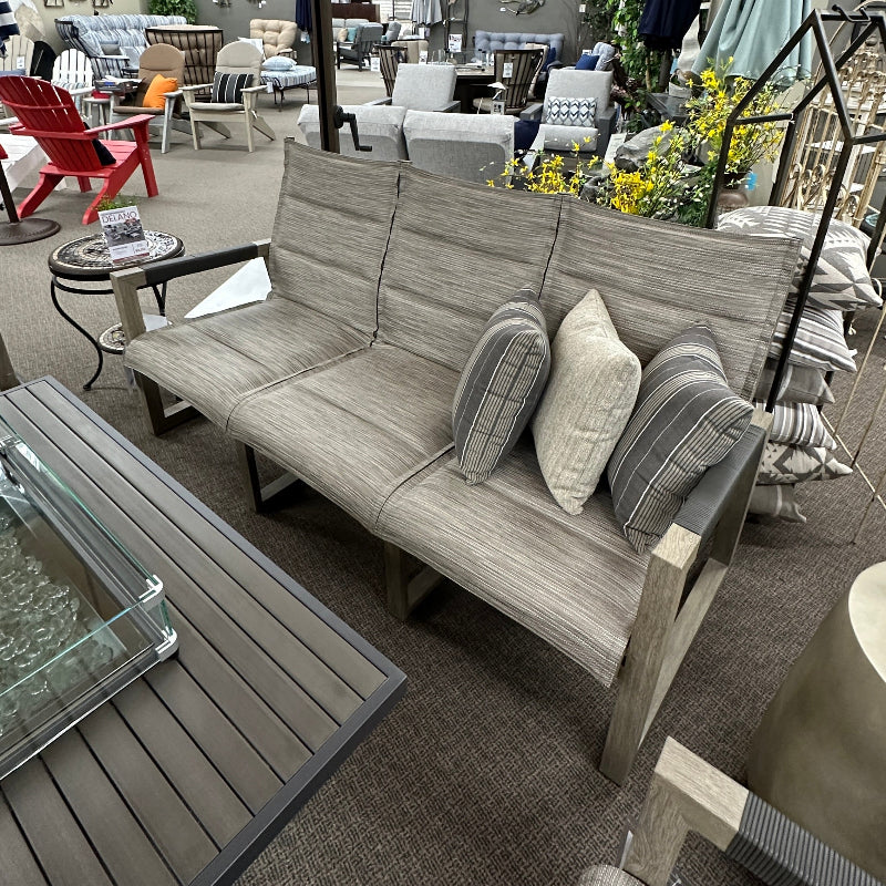 Outdoor furniture set with a gray sofa, chairs, and umbrellas in an indoor showroom.