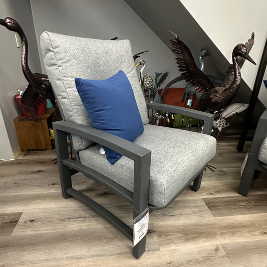 Gray armchair with a blue pillow on a wooden floor, with decorative elements in the background.