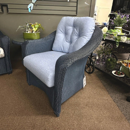 Gray wicker chair with cushioned seat and backrest in a store setting with decor items.