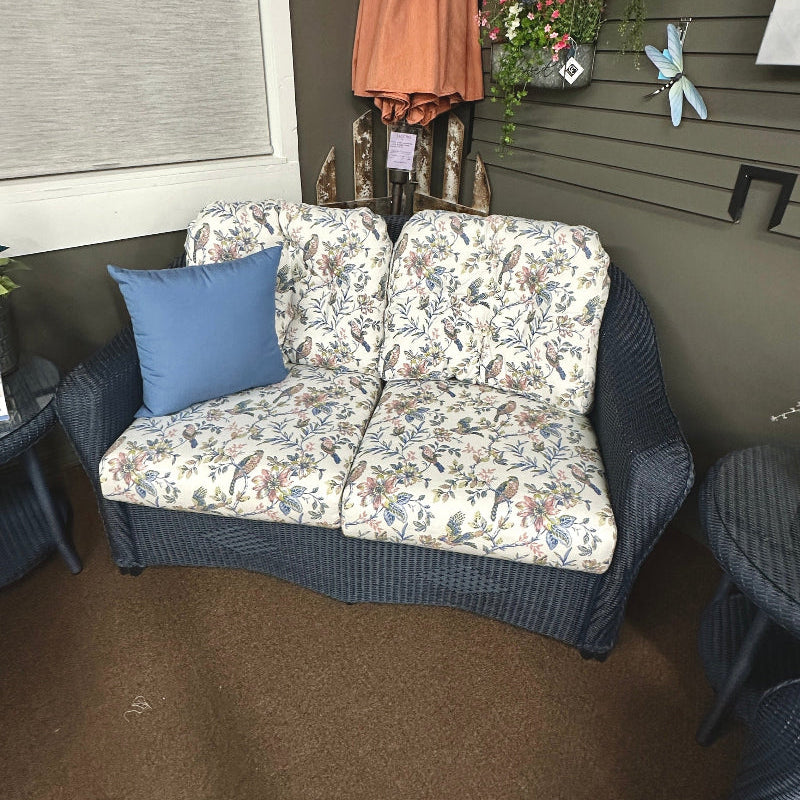 Floral-patterned outdoor sofa with a blue pillow against a wall with decorative items.