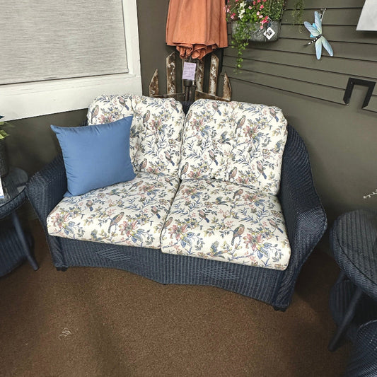 Floral-patterned outdoor sofa with a blue pillow against a wall with decorative items.