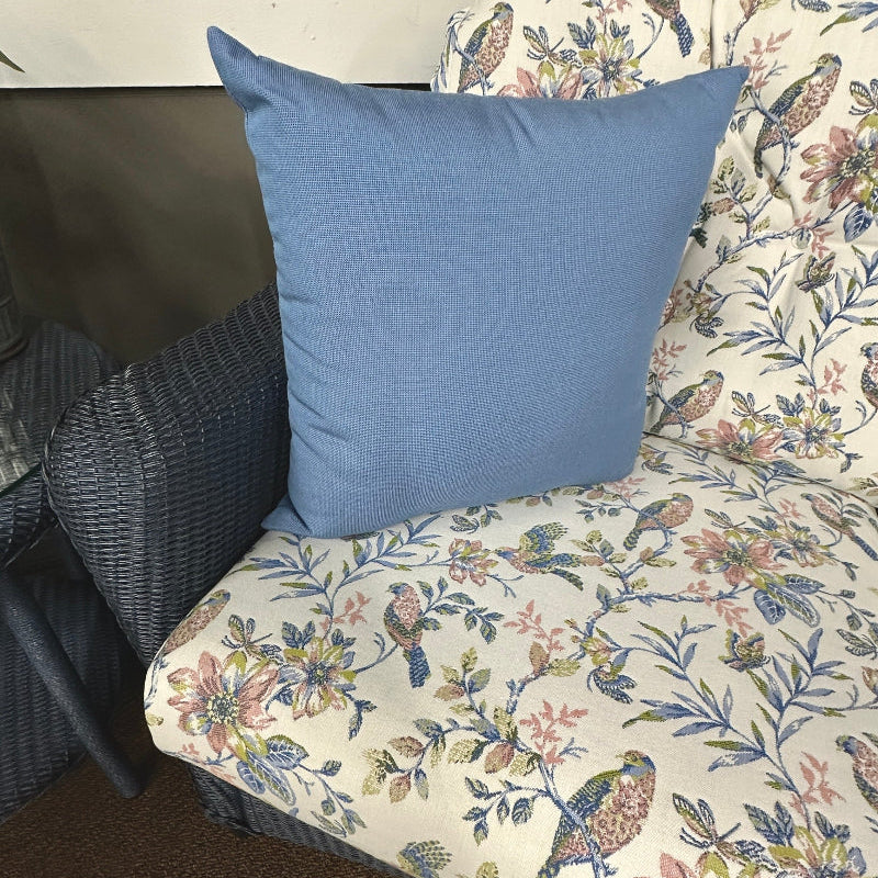 Floral-patterned cushion with a blue pillow on a wicker chair.