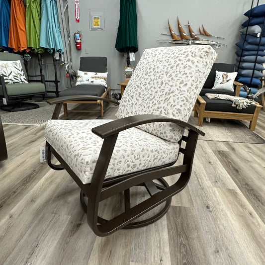 A patio glider chair with a cream and brown floral patterned cushion and a dark brown wooden frame, shown in a furniture store showroom with wood-look flooring.
