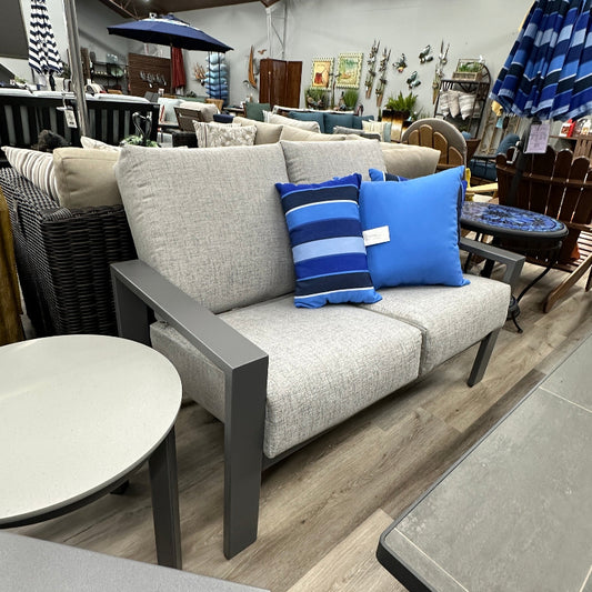 Outdoor furniture set with gray sofa, blue pillows, and tables in a showroom setting.