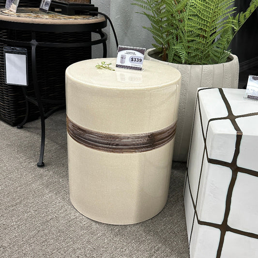 Decorative side table with wicker banding next to a patterned ottoman in an indoor setting.