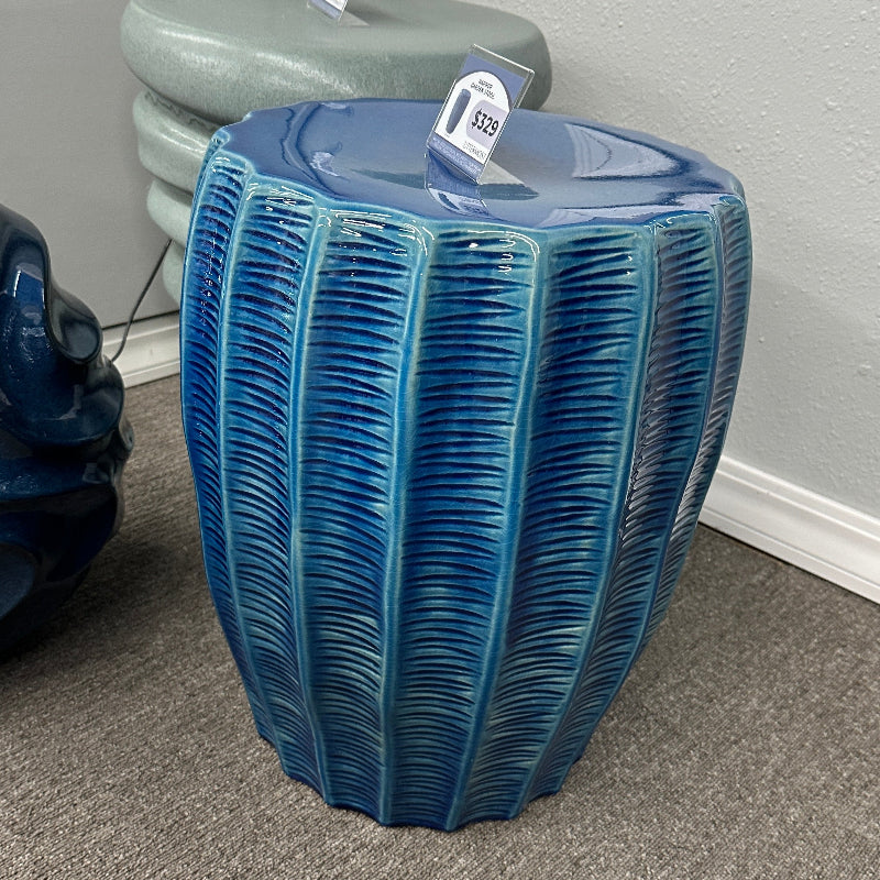 Blue textured side table on a gray carpeted floor with a neutral wall background