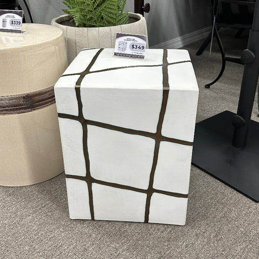 White cube-shaped table with black grid pattern on a gray carpeted floor.