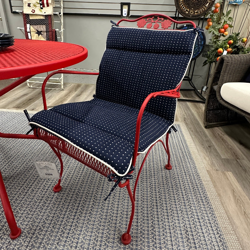 Red metal chair with navy cushion on a patio, surrounded by decorative items.