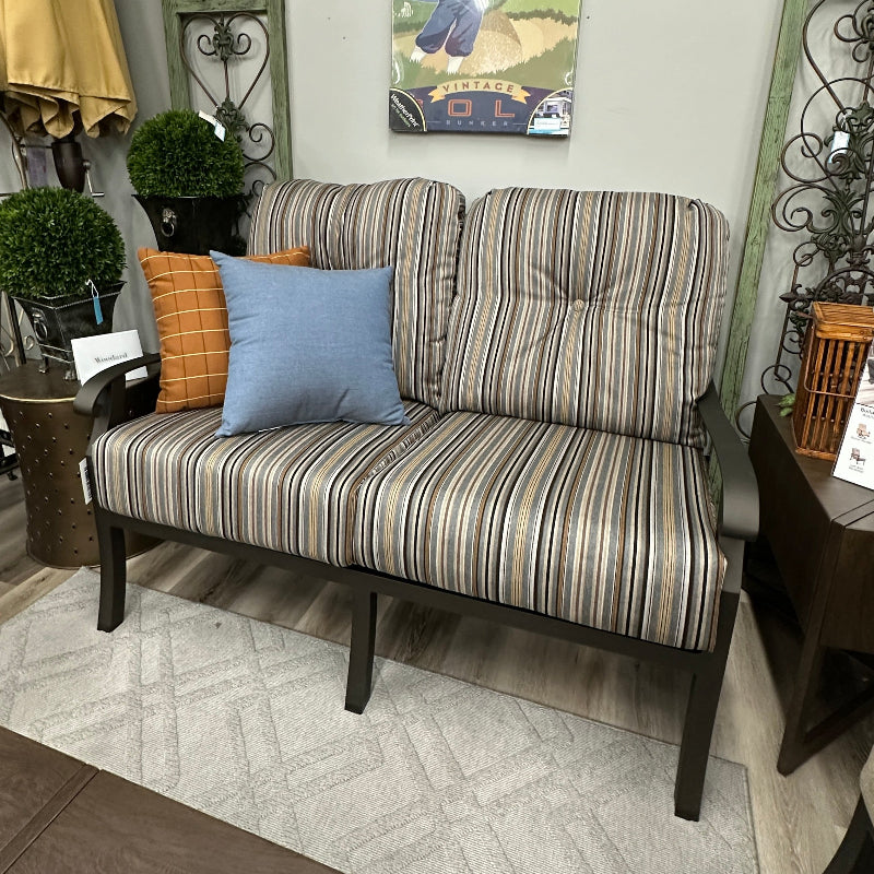 A striped outdoor loveseat sofa with dark wood legs, styled with two accent pillows in a living room setting.