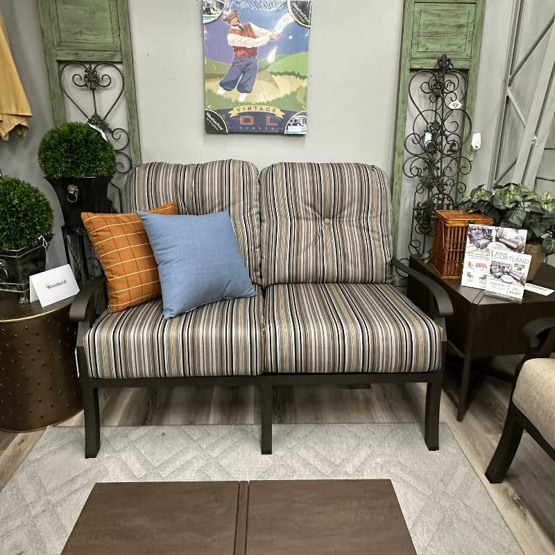 A striped loveseat sofa with dark legs, styled with an orange striped pillow and a light blue pillow in a showroom setting.