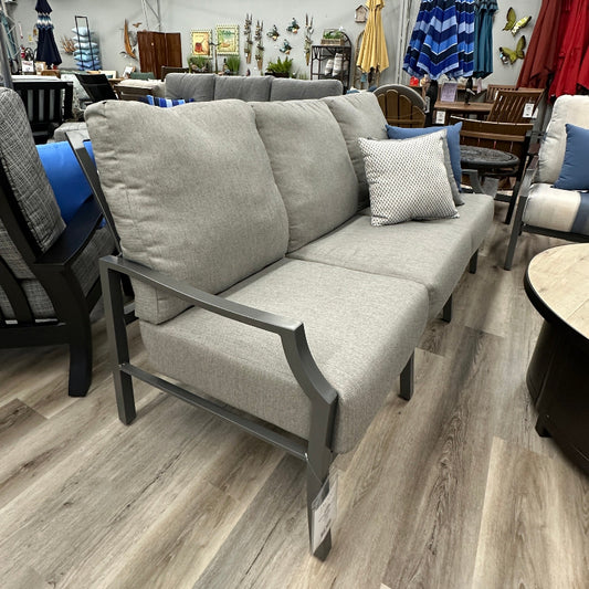 Outdoor furniture set with gray sofa, cushions, and umbrella on a wooden floor.