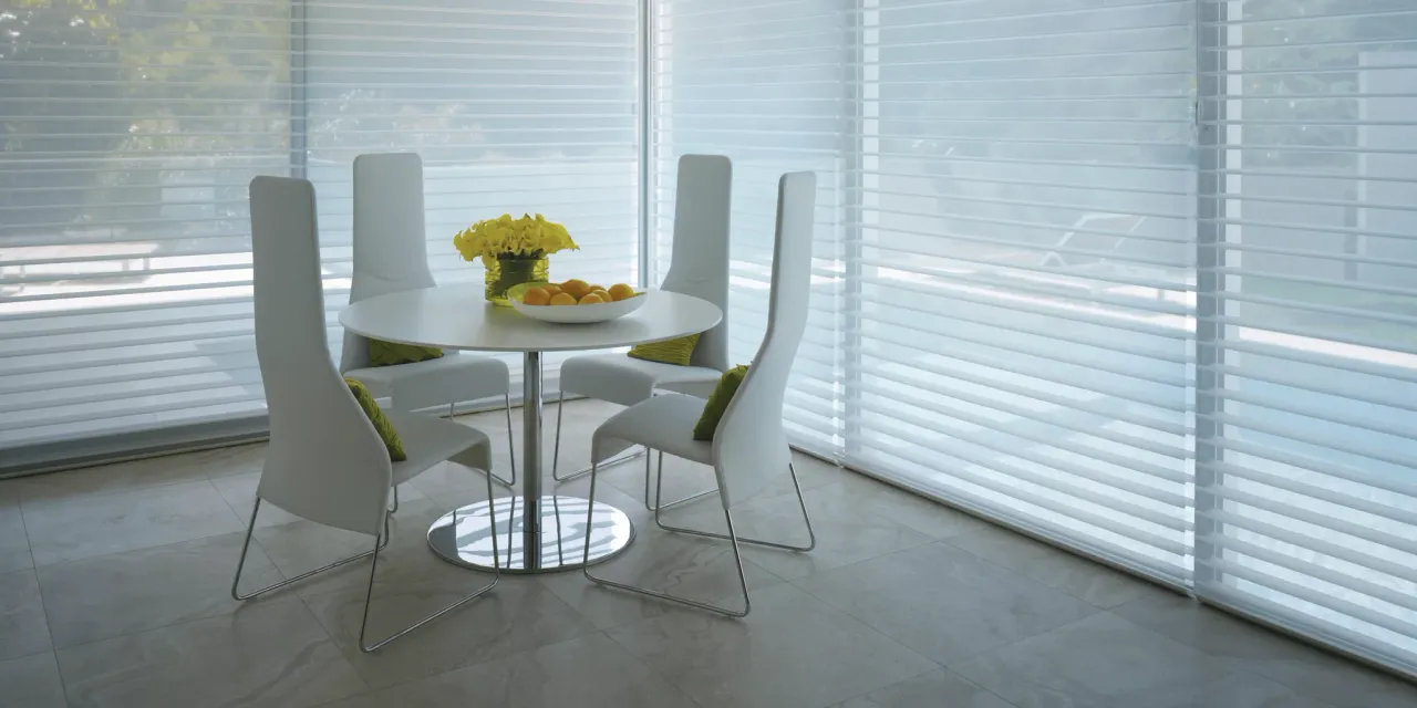 Modern dining room with white chairs and a round table, featuring white window blinds.