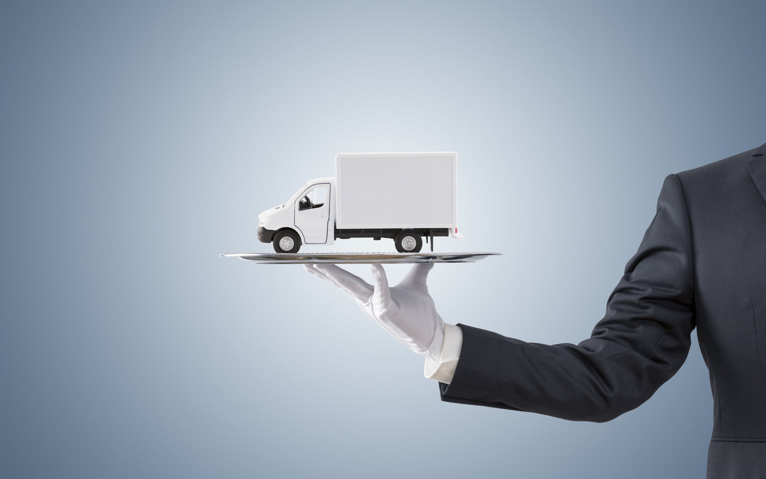 a man wearing a white glove holding a silver tray with a white delivery truck on top of it