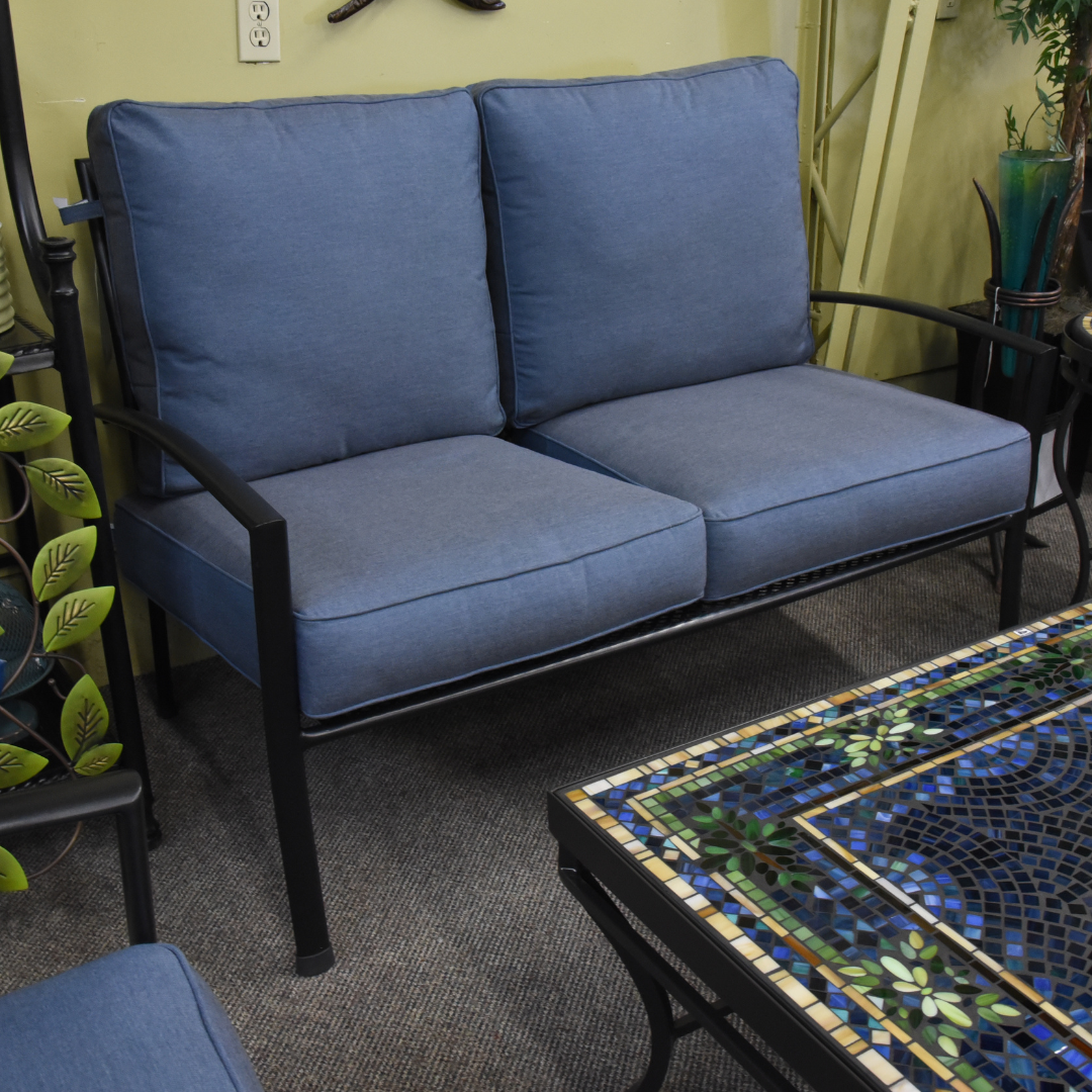 A blue Kettler Reno Patio Club Loveseat with gray cushions placed on a tiled floor in a showroom setting.