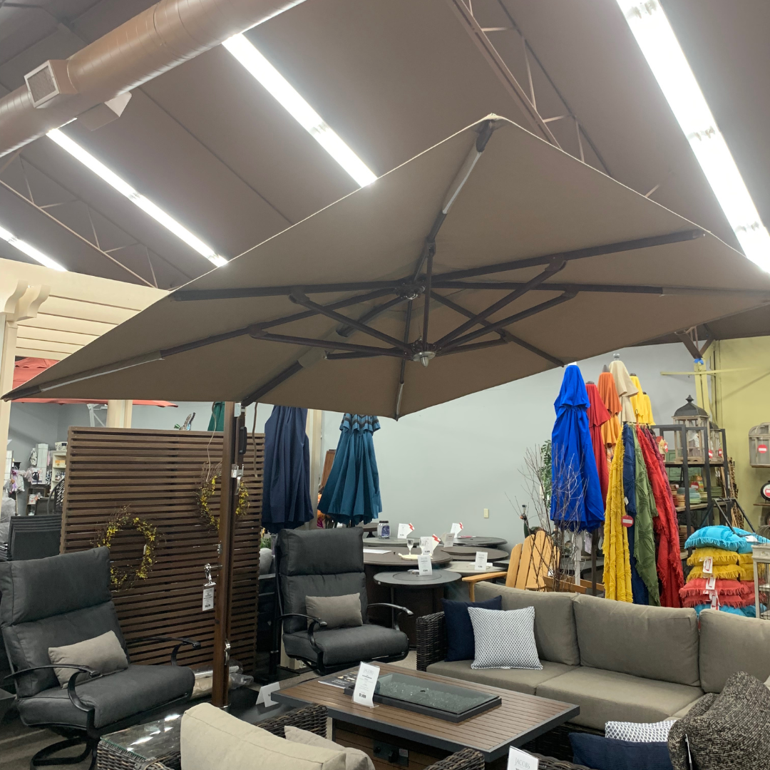 An outdoor umbrella with a square cantilever design, featuring a custom cover, displayed in an indoor setting with various seating arrangements around it.